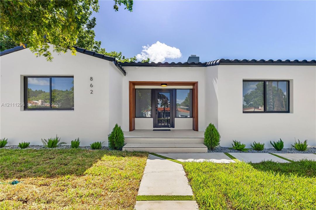 Stucco exterior featuring dark-trimmed windows, a flat tile roof, a wooden-framed entry, and a concrete paver walkway