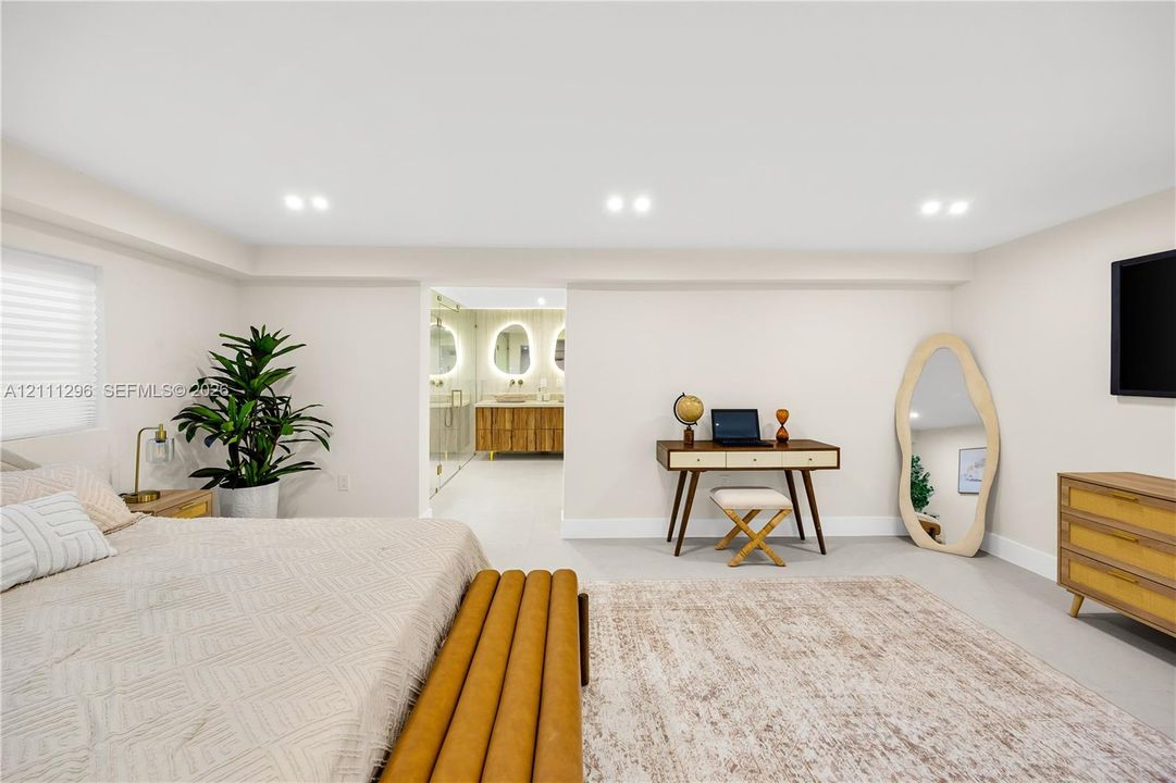 Neutral-toned room featuring recessed ceiling lighting, light-colored tile flooring, and integrated access to a bathroom with a double-sink vanity and illuminated mirrors