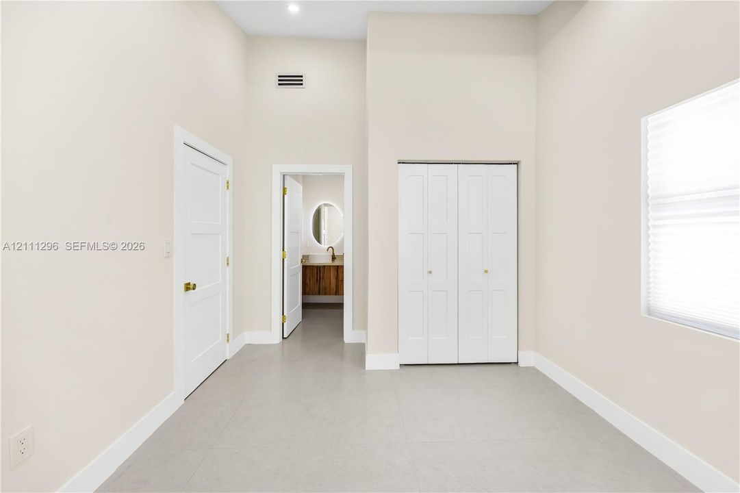 High-ceilinged room featuring neutral wall tones, large-format tile flooring, double-door closet cabinetry, and three-panel interior doors