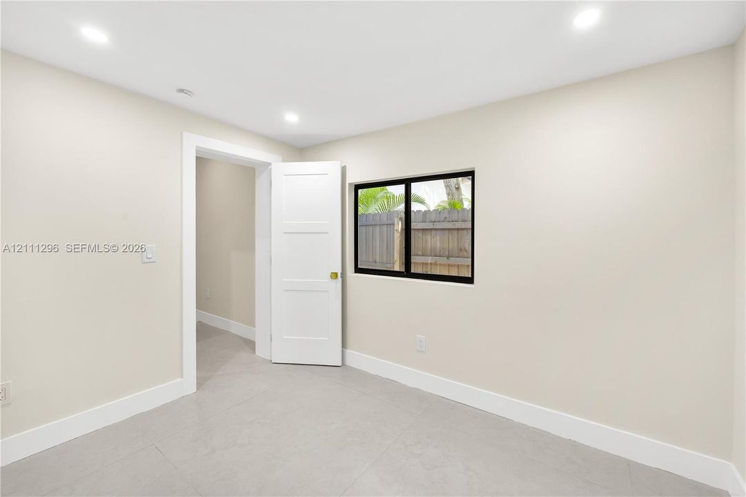 Neutral-toned interior space featuring tile flooring, recessed ceiling lighting, a three-panel interior door, and a black-framed window