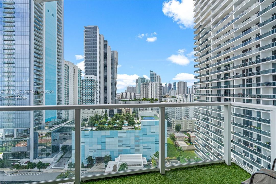 Covered balcony featuring synthetic turf flooring and white metal railings