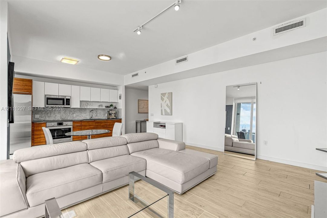 Open-concept kitchen featuring two-tone cabinetry, stone-finish backsplash, built-in stainless steel appliances, and wood-finish flooring