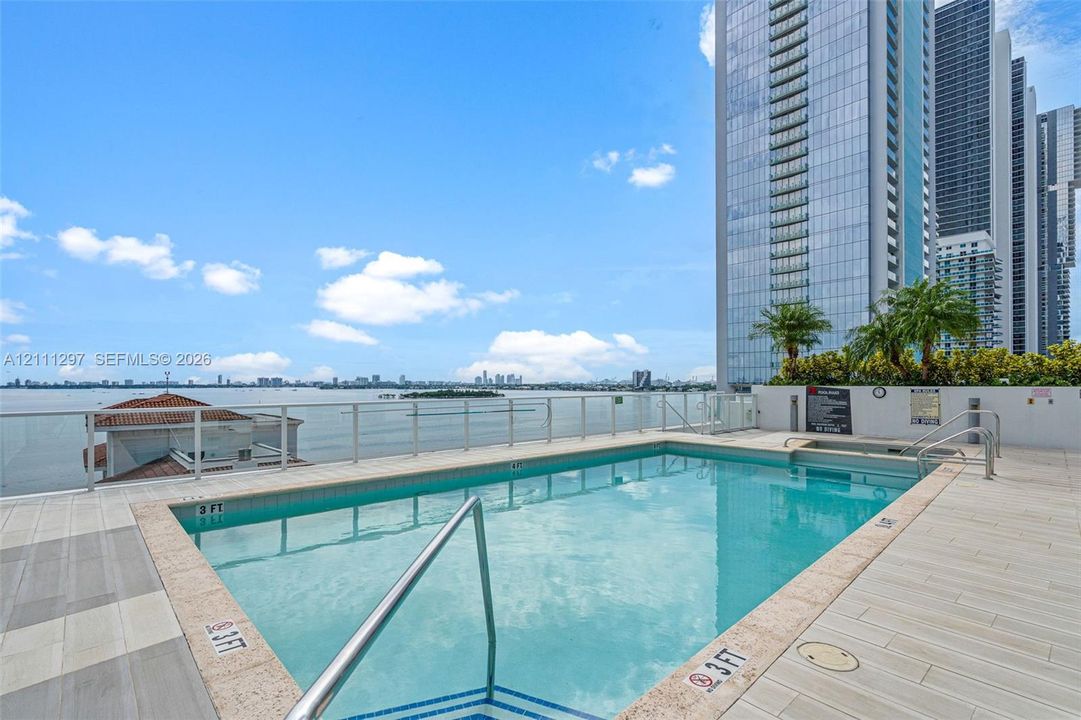 Elevated swimming pool featuring a tile deck, glass panel perimeter railing, integrated spa, and expansive water backdrop