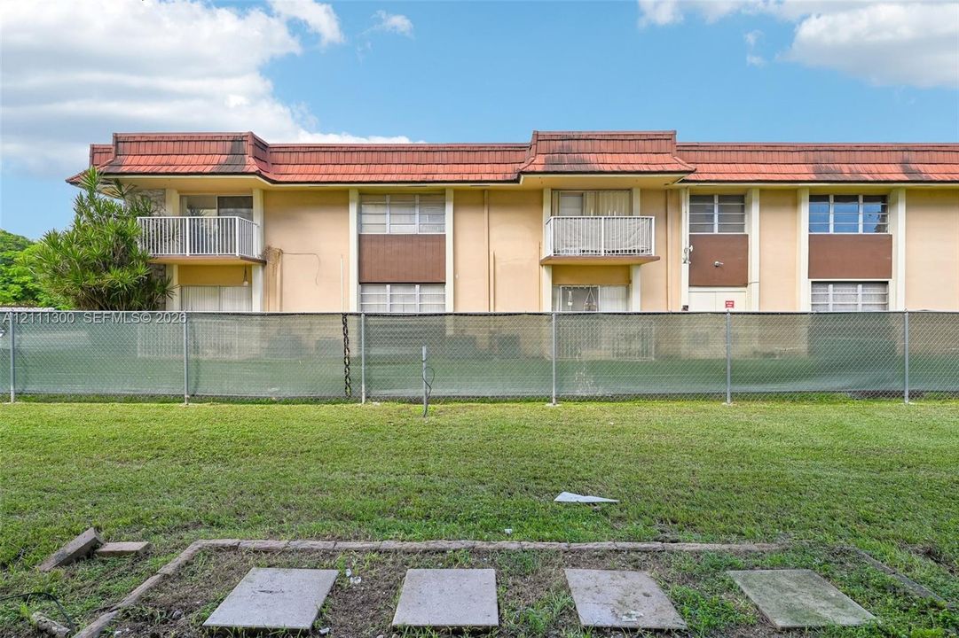 Two-story multi-unit exterior featuring a red tile roof, beige stucco facade, metal balcony railings, and grass lawn