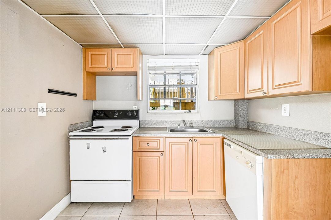 Kitchen featuring light-finish wood cabinetry, speckled laminate countertops, a stainless steel sink, a built-in dishwasher, and an electric range