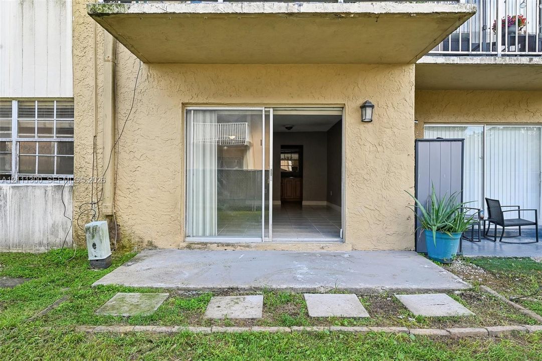 Concrete patio featuring sliding glass door access, exterior wall-mounted light fixture, and stone paver walkway