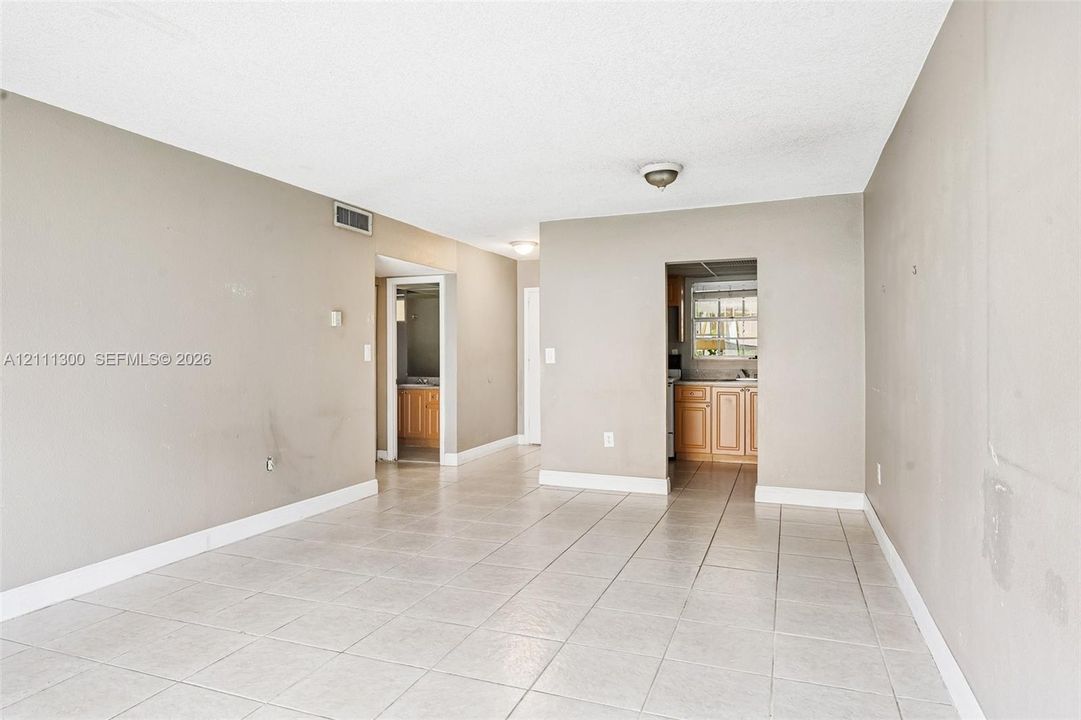 Neutral-toned interior space featuring light-colored ceramic tile flooring, flush-mount lighting fixtures, and visible wood-finish cabinetry in the kitchen area