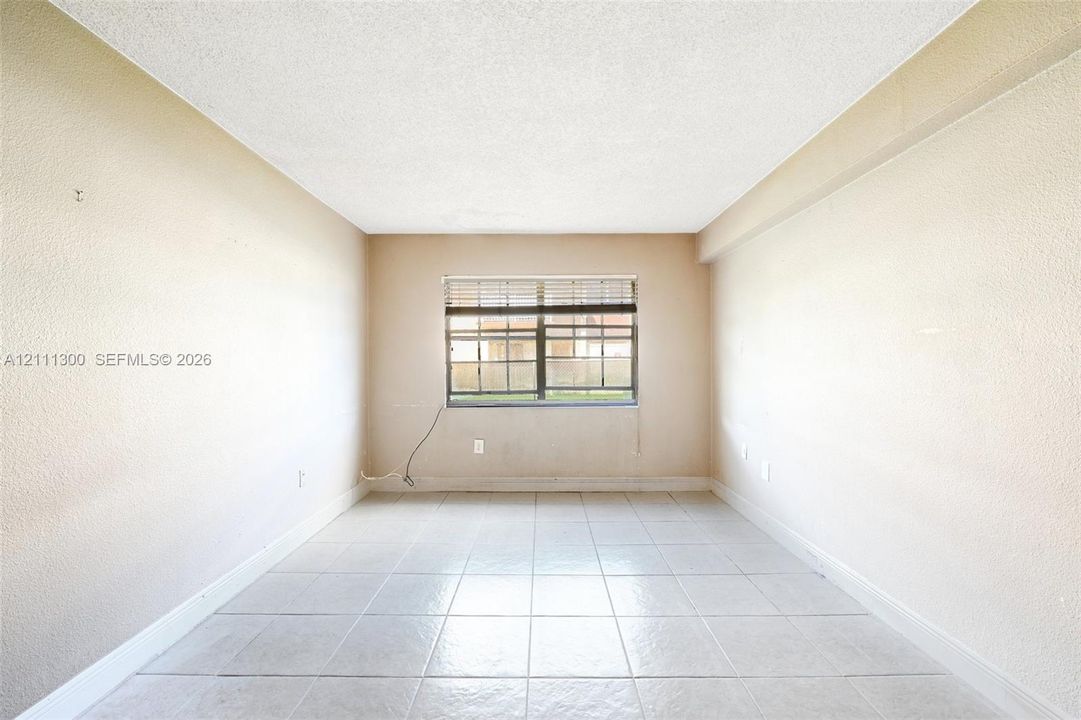 Interior room featuring neutral-toned tile flooring, textured wall finishes, and a single-pane window with adjustable blinds