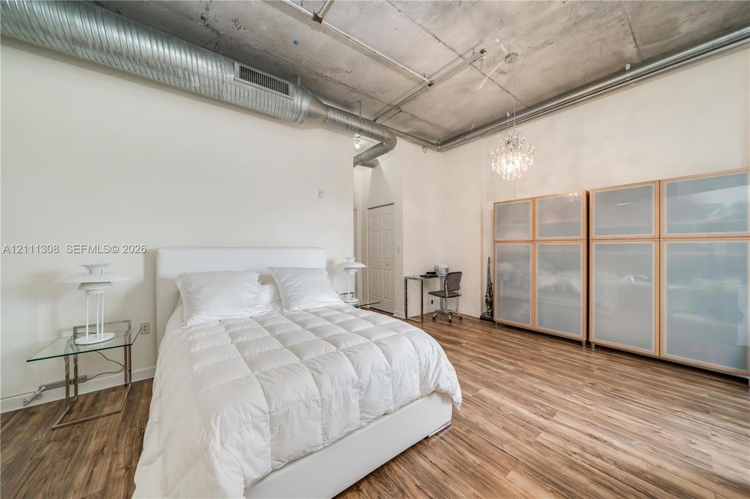 Industrial-style room featuring high concrete ceilings, exposed spiral ductwork, wood-finish flooring, and built-in glass-paneled cabinetry