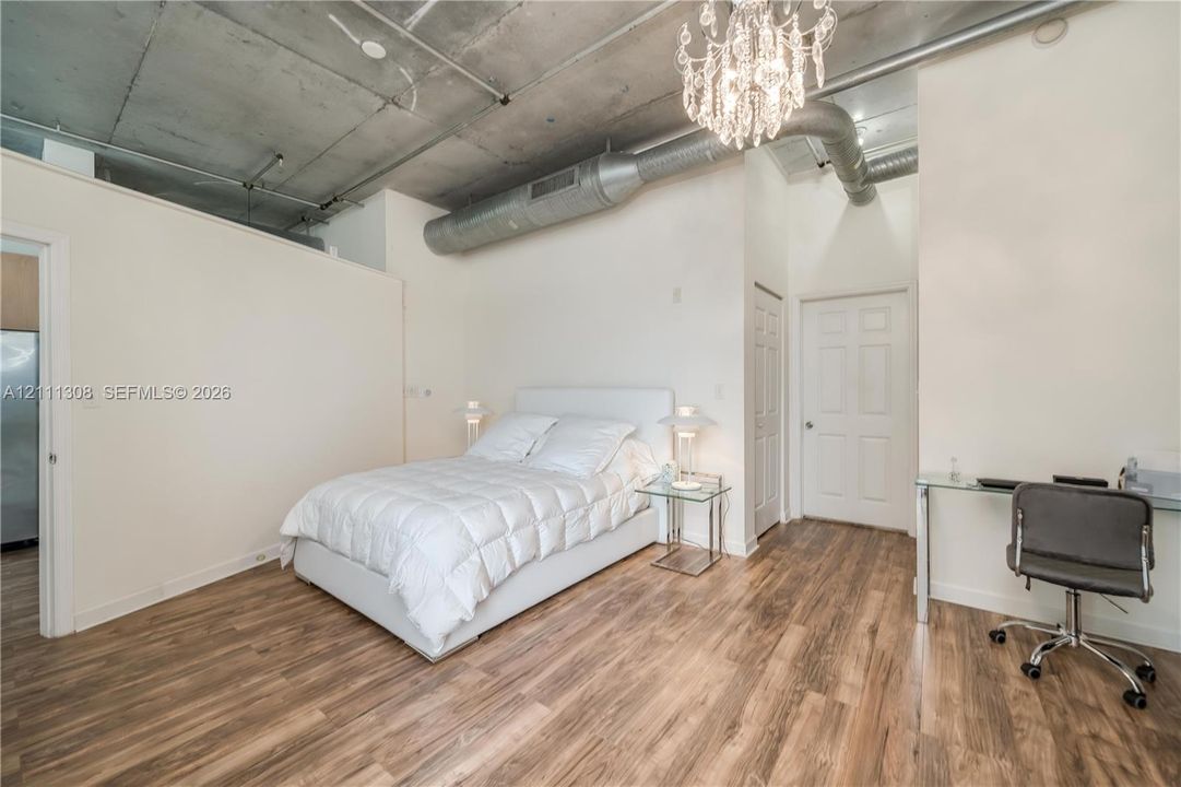 Exposed concrete ceiling with industrial-style ductwork, wood-finish flooring, and a crystal chandelier