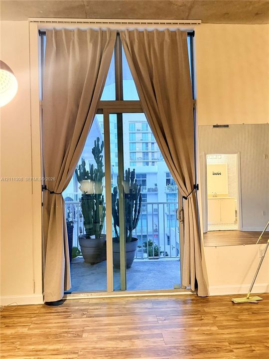 Floor-to-ceiling glass sliding doors, exposed concrete ceiling, wood-finish flooring, and private balcony