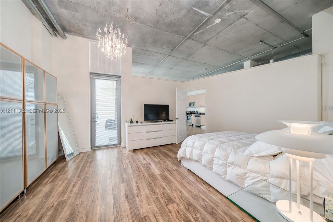 Exposed concrete ceiling, wood-finish flooring, glass-paneled entry door, crystal chandelier, and built-in closet cabinetry