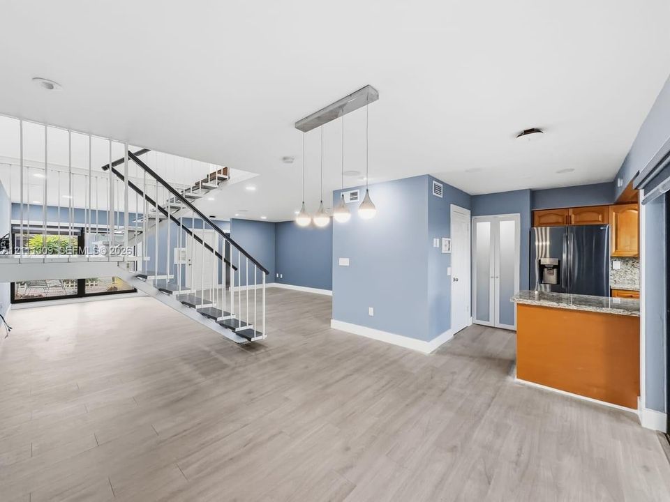 Open-concept interior featuring wood-finish flooring, a custom metal staircase with vertical railings, and a multi-pendant light fixture