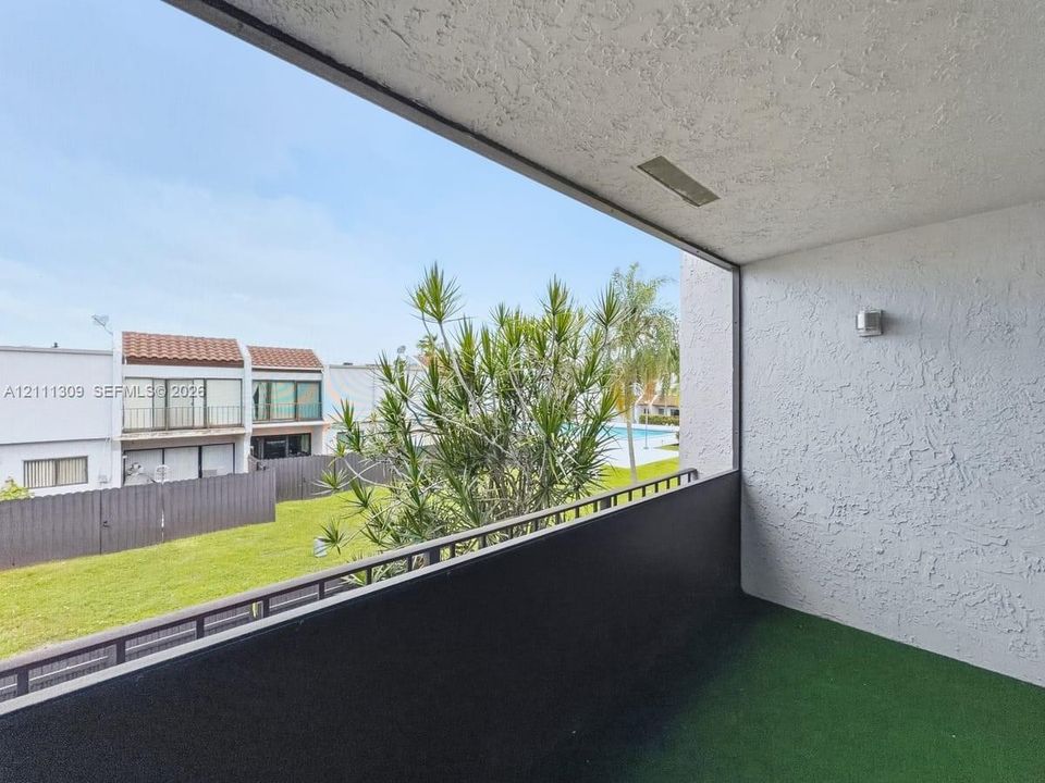 Covered balcony featuring textured stucco walls, a dark metal railing, and an exterior wall-mounted light fixture