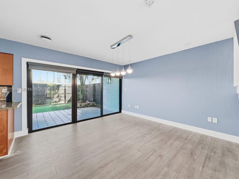 Expansive multi-panel sliding glass door, wood-finish flooring, linear four-light pendant fixture, and hardscaped patio