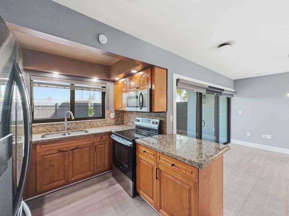 Kitchen featuring wood cabinetry, stone-finish countertops, stainless steel appliances, wood-finish flooring, and sliding glass doors