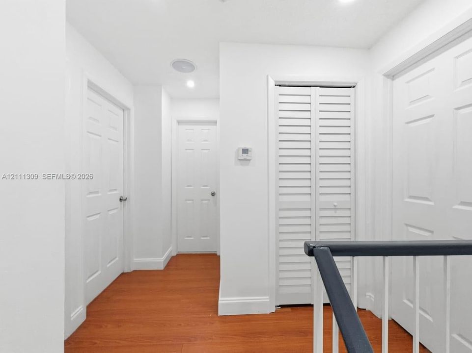 Hallway featuring wood-finish flooring, six-panel interior doors, louvered closet doors, and a contrasting handrail with vertical balusters