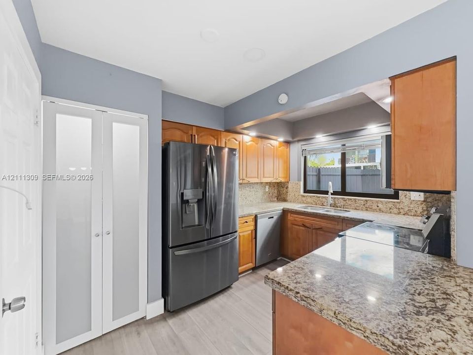Kitchen featuring wood cabinetry, stone countertops, stainless steel appliances, a double-basin sink, and frosted-glass pantry doors