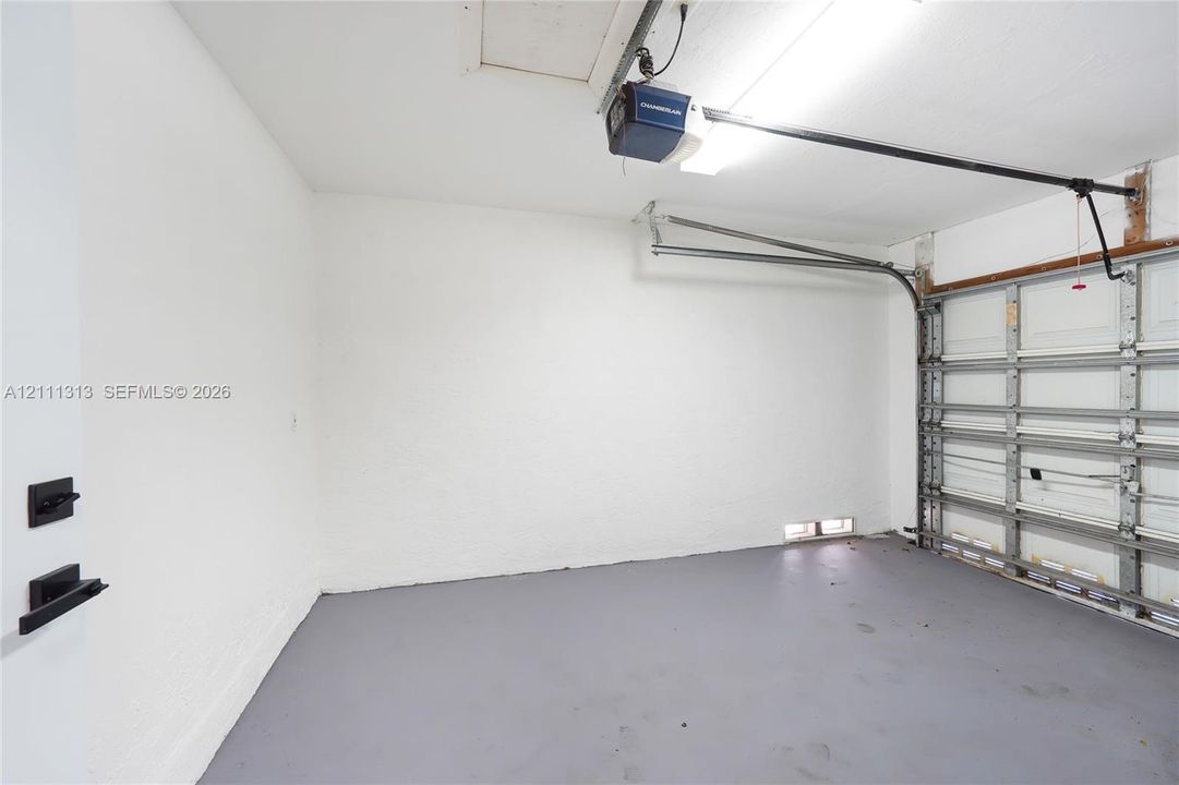 Garage space featuring painted concrete flooring, textured white walls, a motorized door opener, and metal garage door hardware
