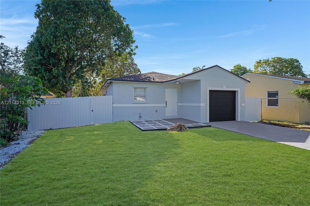 Single-story residence featuring a light-toned stucco exterior, a concrete driveway, an attached garage with a dark-finished door, and a privacy fence