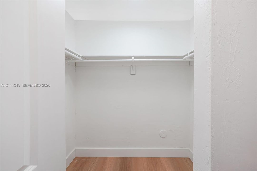 Walk-in storage space featuring wood-finish flooring and built-in shelving with integrated rods