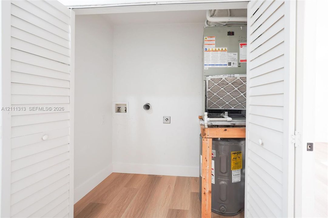 Utility closet featuring wood-finish flooring, white louvered bi-fold doors, water heater, and HVAC system