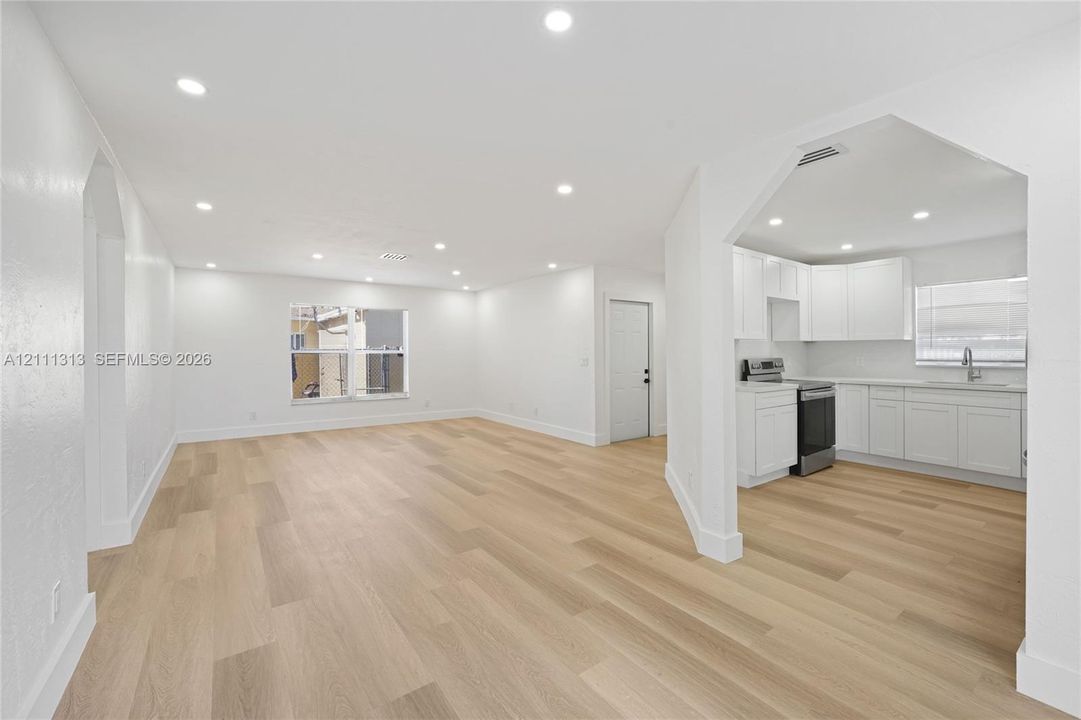 Open-concept living space featuring wood-finish flooring, recessed lighting, white cabinetry, integrated stainless steel appliances, and quartz countertops