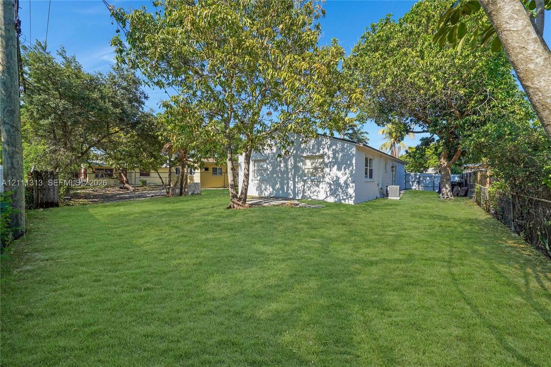 Expansive backyard featuring a large grass lawn, mature trees, and perimeter fencing