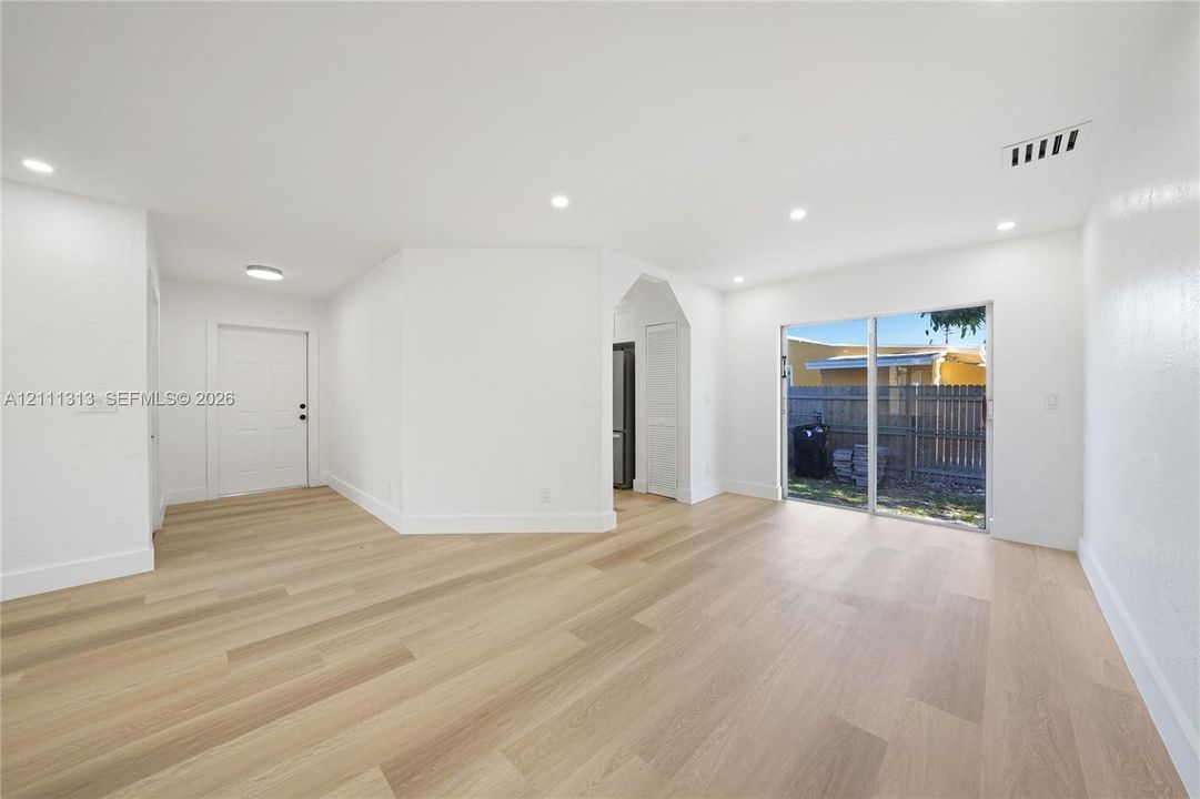 Open-concept interior space featuring light wood-finish flooring, recessed lighting, smooth white walls, and a sliding glass door providing external access