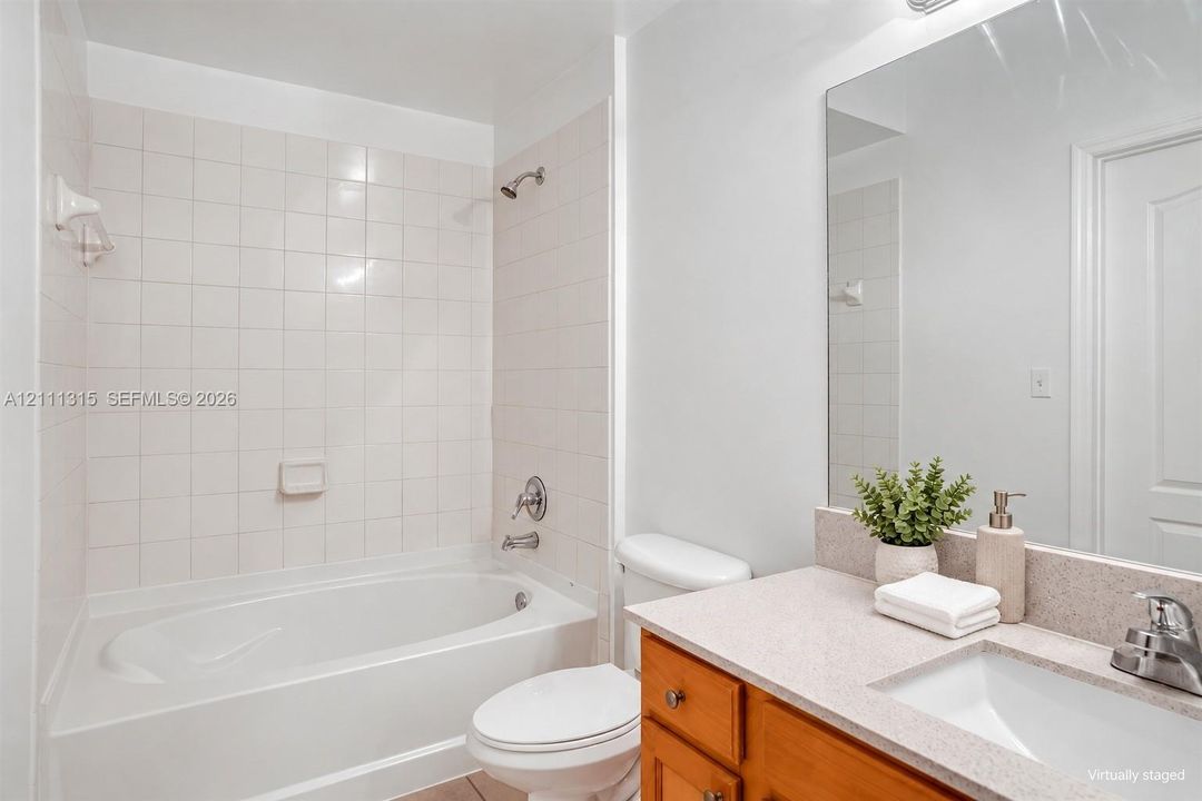 Bathroom featuring a shower-tub combination with white tile surround, wooden vanity cabinet, solid-surface countertop with an integrated sink, and a large wall-mounted mirror