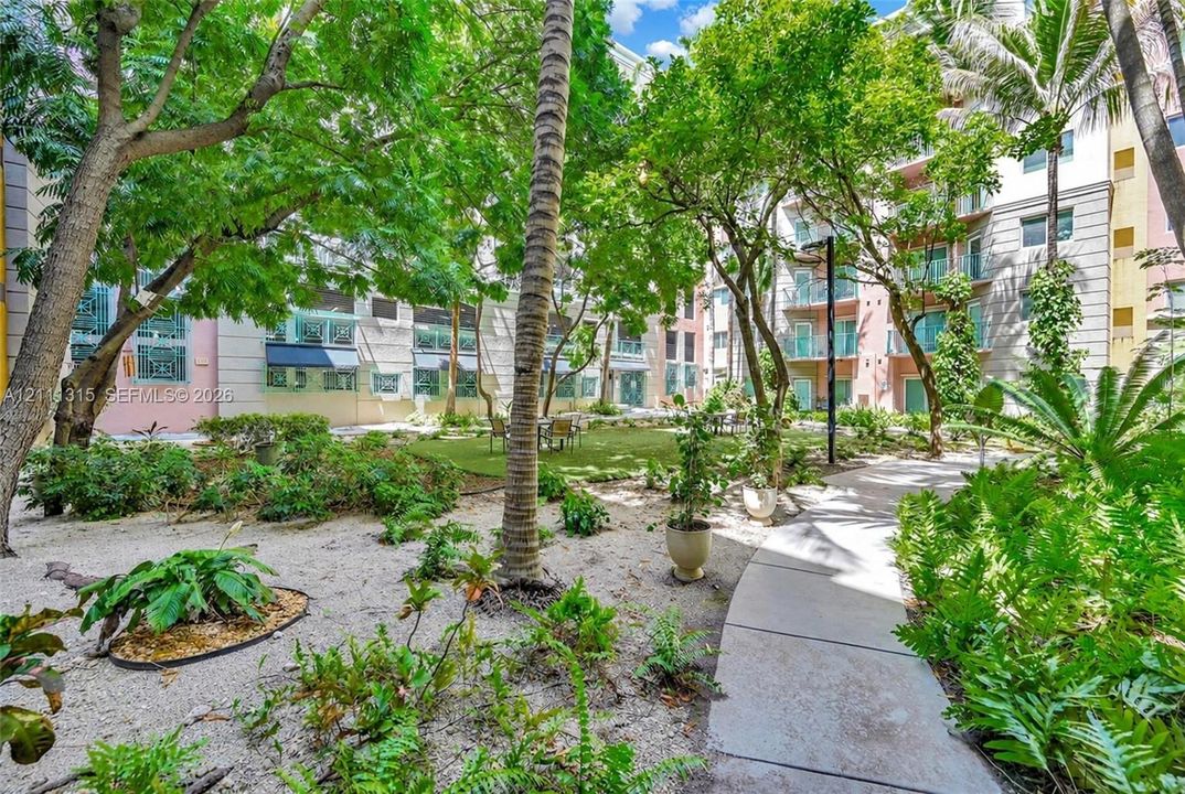 Courtyard featuring mature tropical trees, manicured landscaping, gravel garden beds, and a concrete pathway