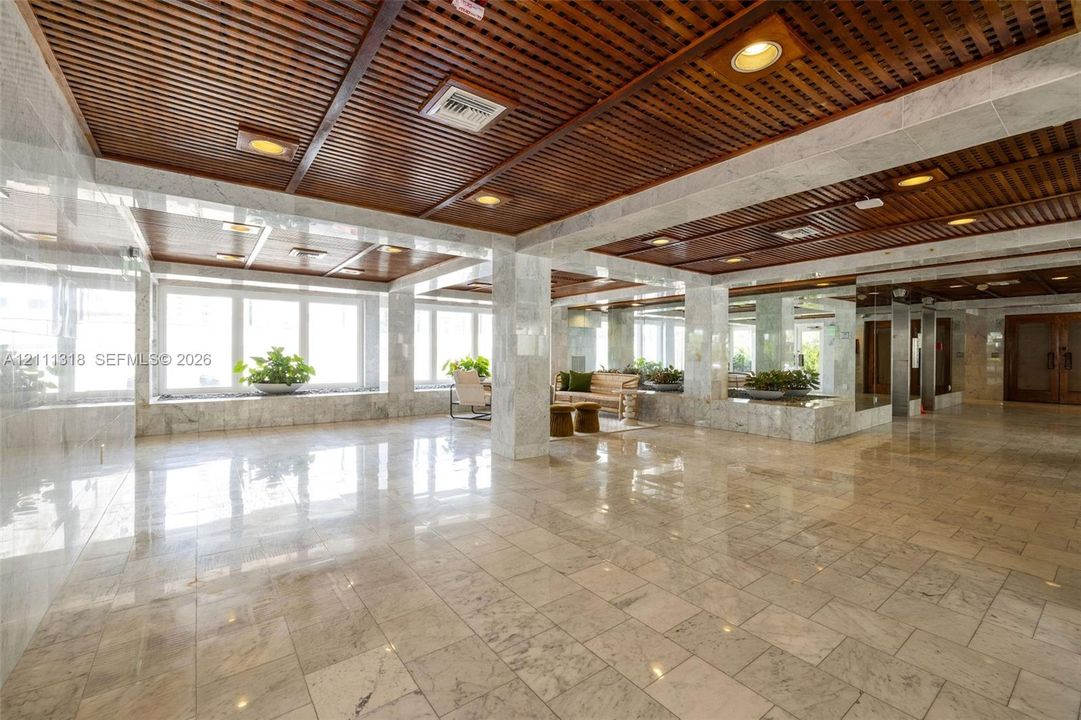Expansive lobby featuring polished stone flooring, wood-slat ceiling, recessed lighting, floor-to-ceiling windows, and integrated stone-surround planter ledges