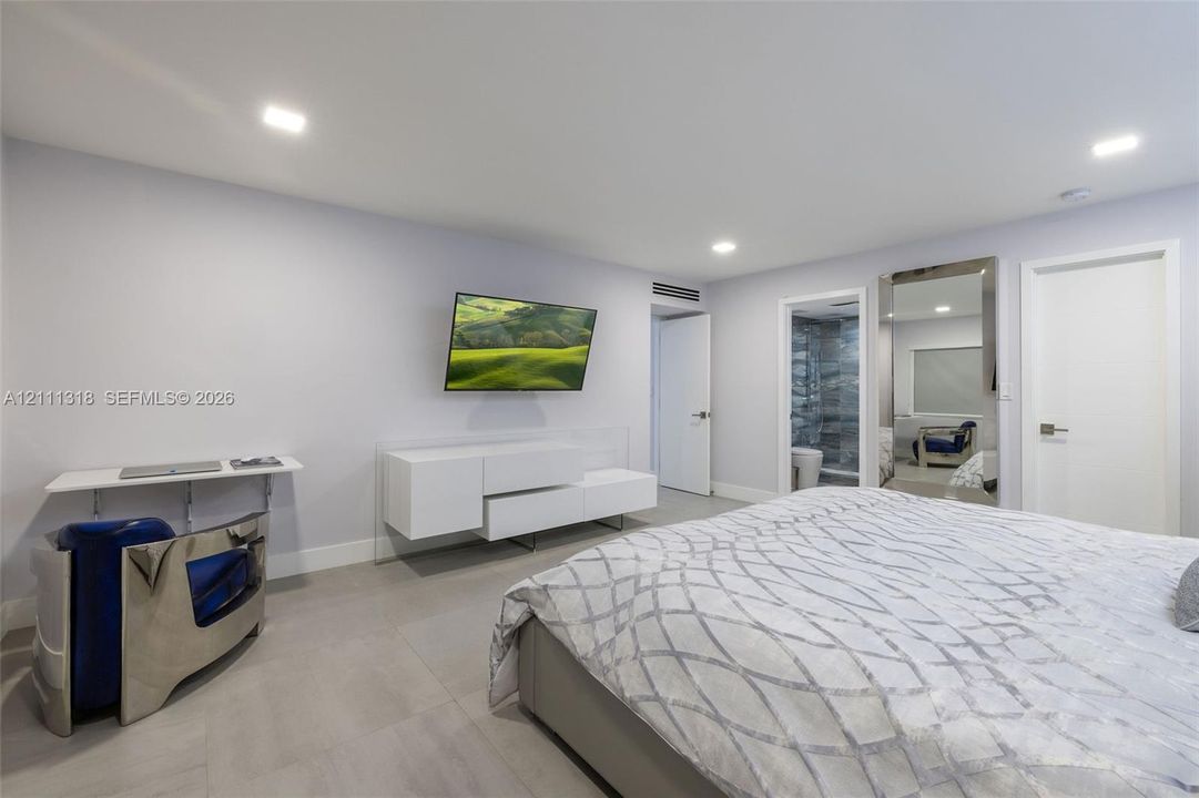 Neutral-toned room featuring large-format tile flooring, recessed ceiling lighting, and a wall-mounted white media console