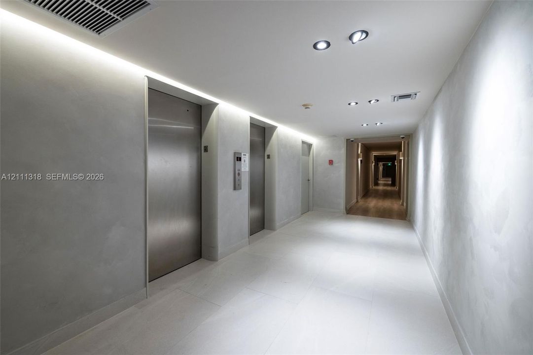 Modern lobby featuring brushed stainless steel elevators, recessed ceiling lighting, cove lighting, and large-format tile flooring