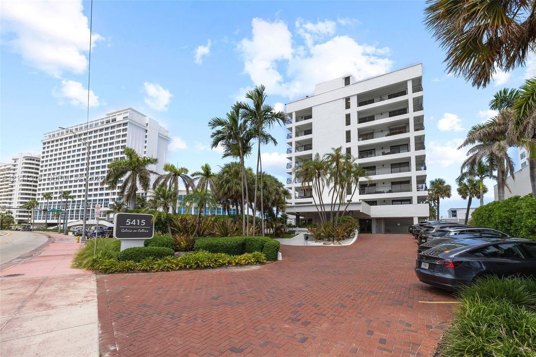 Multi-story residential building featuring a brick-paved circular driveway, structured balconies, and mature palm landscaping