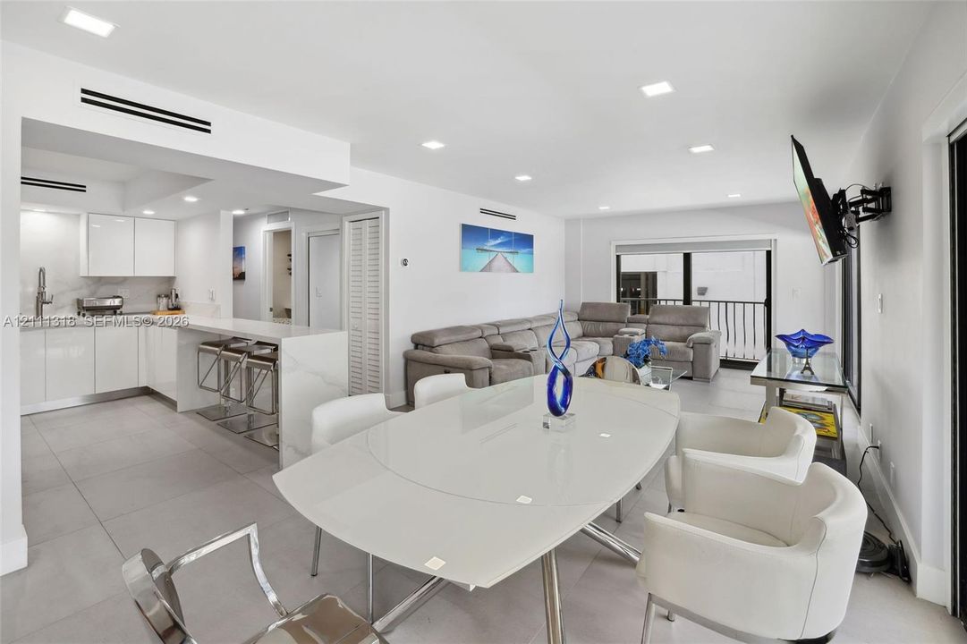 Open concept area featuring high-gloss cabinetry, stone-surface breakfast bar, large-format tile flooring, recessed lighting, and built-in HVAC registers