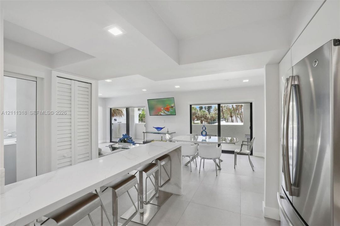 Kitchen featuring a stone-surface waterfall peninsula, stainless steel refrigerator, large-format tile flooring, recessed lighting, and sliding glass doors