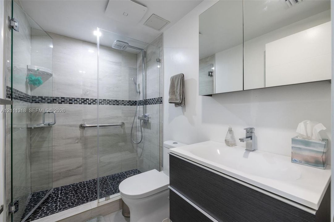 Bathroom featuring a walk-in shower with glass enclosure, pebble-stone flooring, mosaic tile accents, wall-mounted shower hardware, and a vanity with a rectangular sink and integrated cabinetry