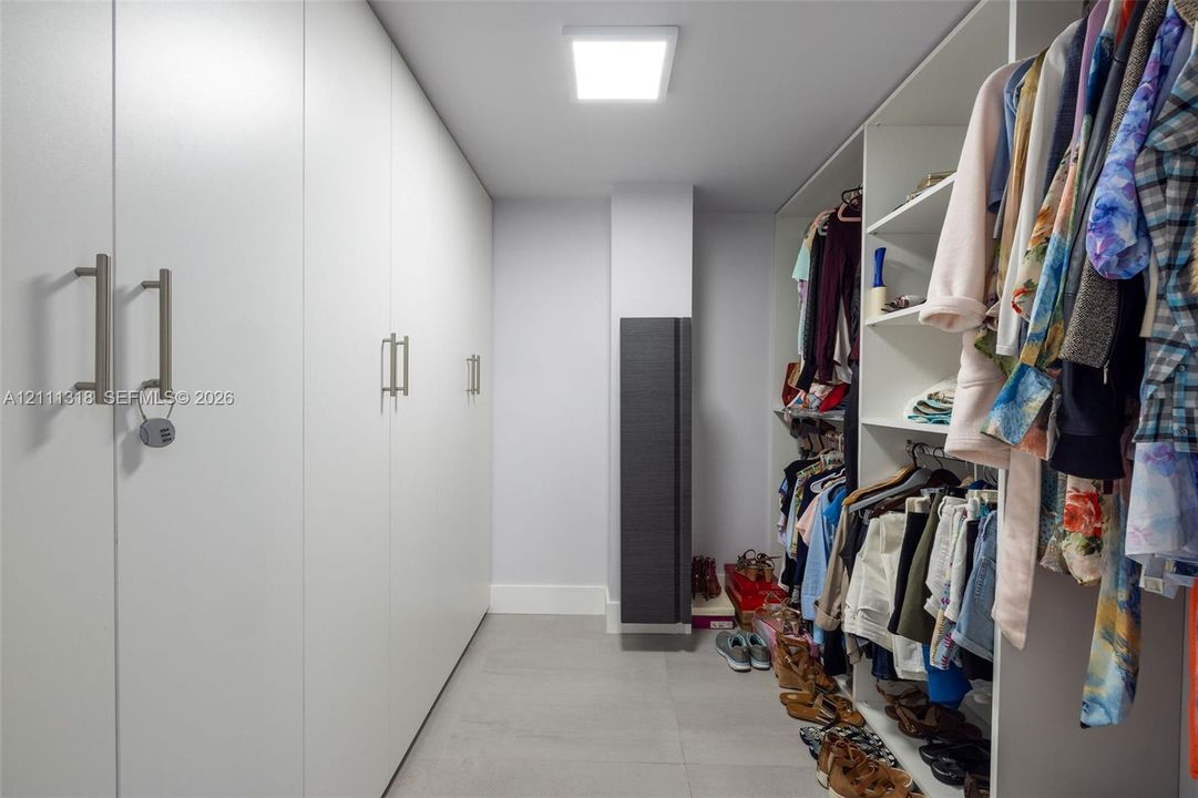 Custom storage area featuring floor-to-ceiling cabinetry with brushed-finish hardware, open shelving, tile flooring, and a flat-panel flush-mount ceiling light