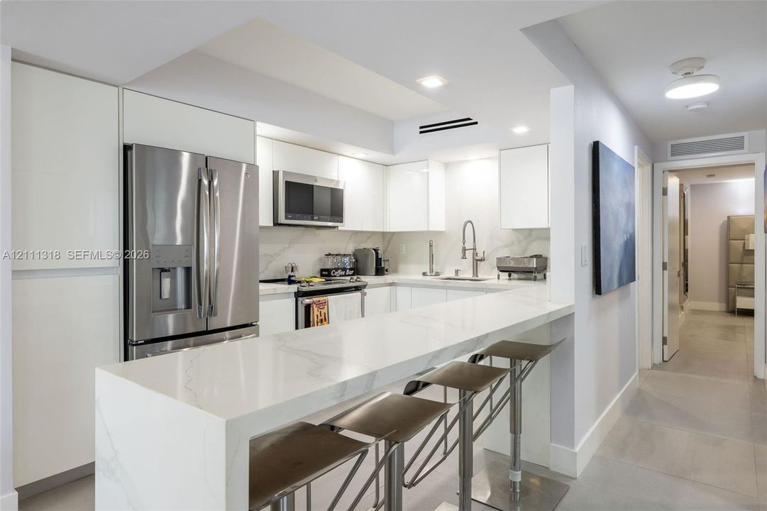 Kitchen featuring white flat-panel cabinetry, a waterfall-edge stone countertop with a breakfast bar, stone slab backsplash, and stainless steel appliances