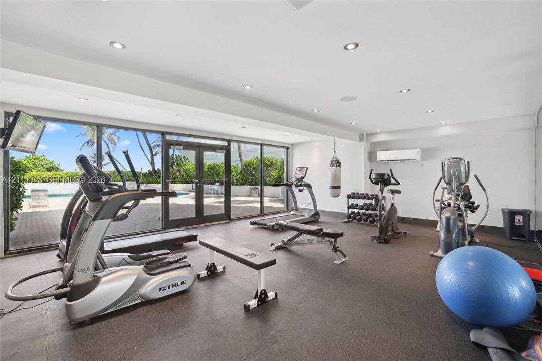 Fitness center featuring recessed lighting, dark composite flooring, wall-mounted ductless climate control, and full-height glass doors providing direct access to the exterior patio