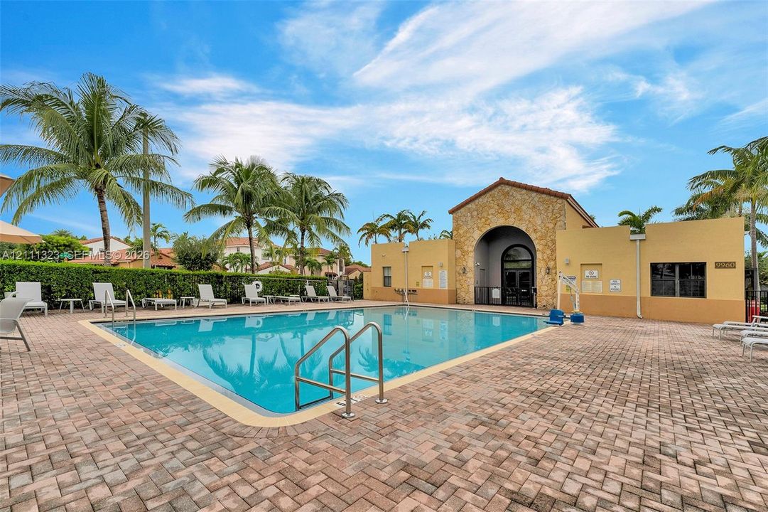 Swimming pool featuring a stone-accented clubhouse, brick-paver pool deck, and mature palm trees