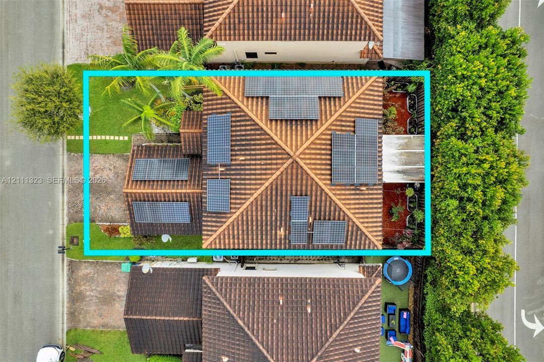 Aerial view of property featuring a tile roof equipped with a solar panel array, manicured landscaping, and mature palm trees