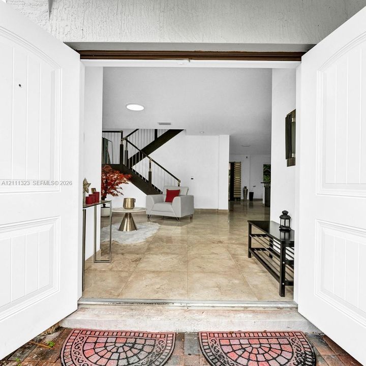 Double entry doors opening to a large-format tile foyer featuring an open-riser staircase with metal railings