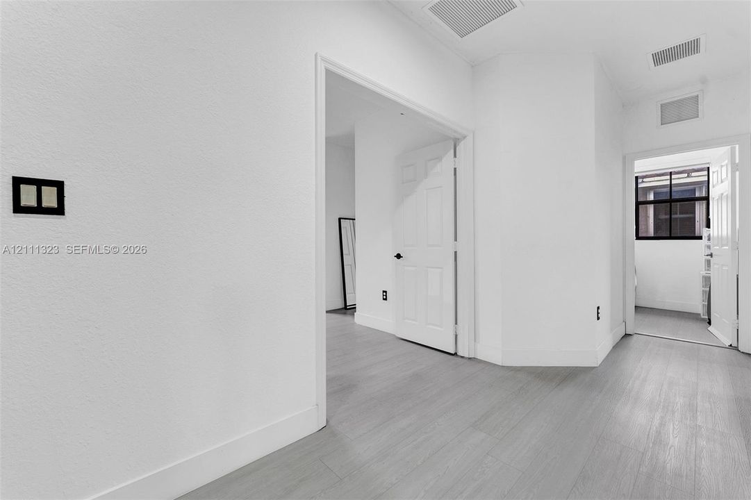 Interior space featuring wood-finish flooring, white walls, and paneled interior doors with matte black hardware