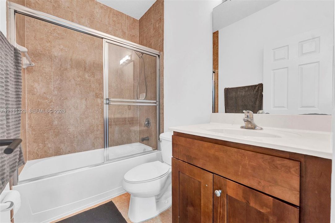 Bathroom featuring a single-sink vanity with wood cabinetry, integrated basin, chrome faucet, and a combination tub and shower with sliding glass doors and neutral-toned wall tile