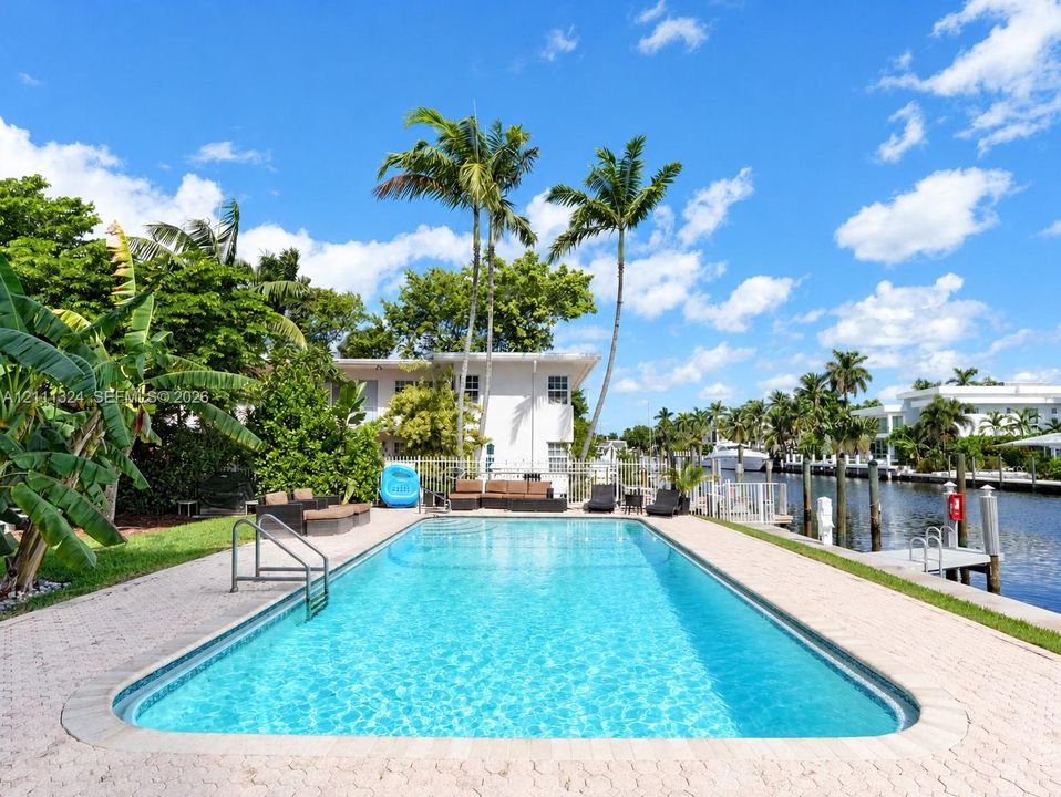 Rectangular in-ground swimming pool with integrated metal handrails, paver stone pool deck, and direct water frontage featuring a private dock