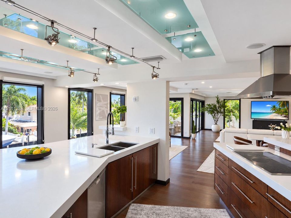 Kitchen featuring  wood-finish cabinetry, solid-surface countertops, track lighting with glass accent panels, a stainless steel range hood, and wood-finish flooring