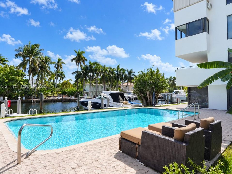 Waterfront swimming pool with paver decking, metal handrails, and direct bulkhead access to a canal