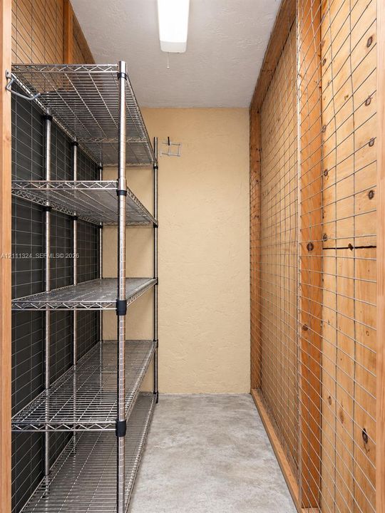 2nd Storage space featuring metal wire shelving, plywood-paneled walls with wire grid overlays, and concrete flooring